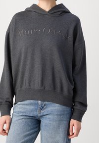 Sudadera con capucha de color gris oscuro, con el logo "Marc O'Polo" en relieve, corte relajado, puños y dobladillo de punto, textura de tela suave. Combinada con jeans claros.
