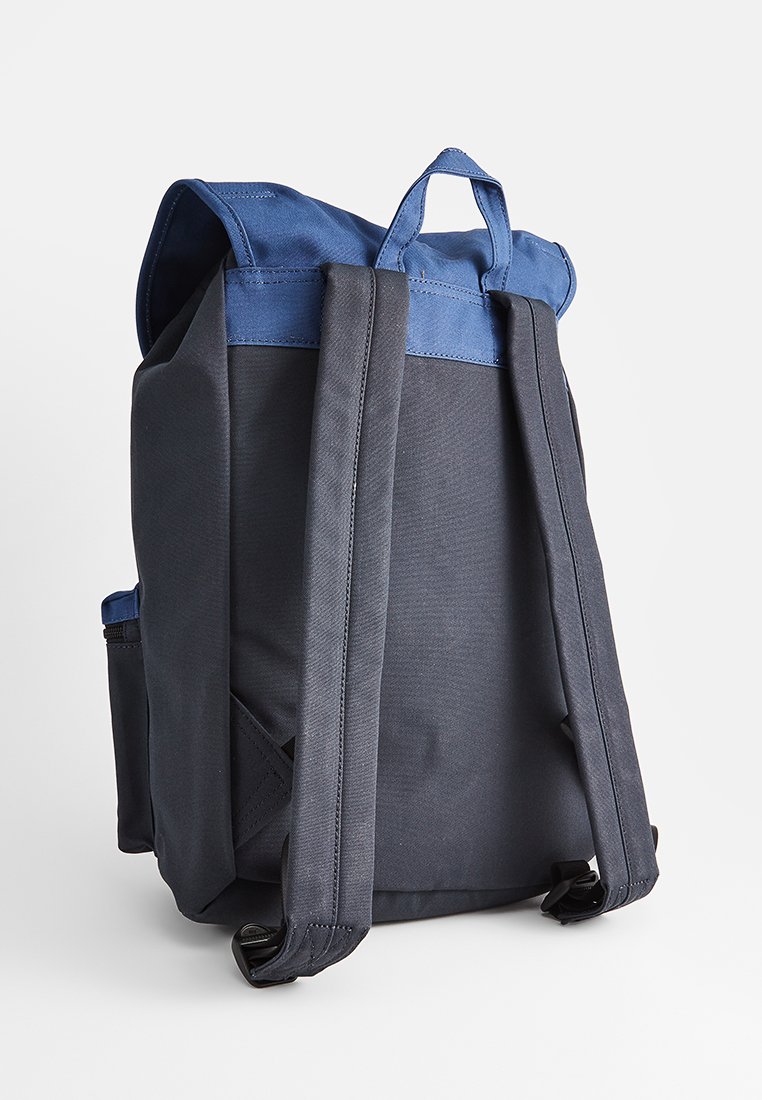Donkerblauw en zwart stoffen rugzak met een gestructureerd ontwerp, bovenhandgreep en twee verstelbare schouderbanden. Bevat een zijvak en een ritsluiting.