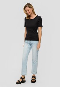 Zwarte korte mouwen gebreide top met een ronde hals, gecombineerd met lichtblauwe rechtvallende jeans en zwarte sandalen met platform en bandjes.
