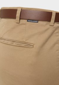 Khaki bukser med et brunt syntetisk læderbælte. Har en enkelt baglomme og et "JACK&JONES" mærke nær taljen.