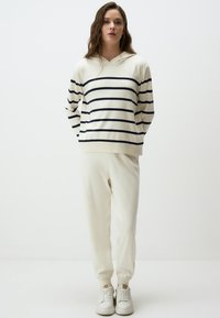 Striped pullover in cream and navy, featuring a hood and long sleeves; paired with matching cream jogger pants and white sneakers.