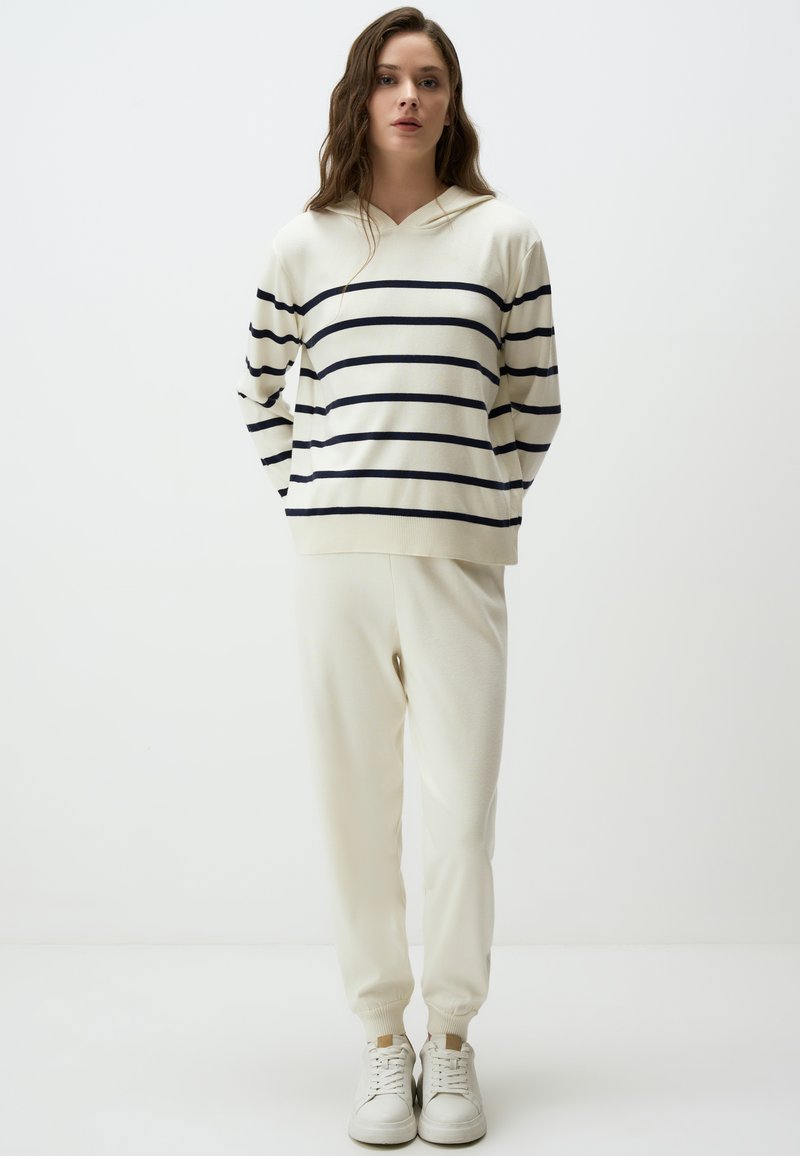 Striped pullover in cream and navy, featuring a hood and long sleeves; paired with matching cream jogger pants and white sneakers.