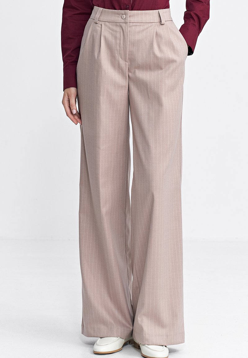 Jasnoróżowe, szerokie spodnie z pionowymi prążkami, z wysokim stanem, bocznymi kieszeniami i gładką fakturą. Połączone z białym obuwiem.