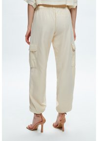 Crème cargobroek met een elastische tailleband, zijzakken en taps toelopende benen. Gekocht met nude hoge hakken. Gladde textuur.