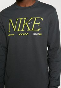 Schwarzes Nike-Shirt mit langen Ärmeln, das auffälligen gelben Text und grafische Akzente zeigt. Es ist aus weichem Material gefertigt und hat ein Rundhalsausschnittdesign.