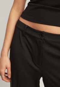 Melni bikses ar gludu tekstūru, pogu aizdari un jostu cilpiņām, ar pieguļošu piegriezumu un sānu kabatas detaļām.