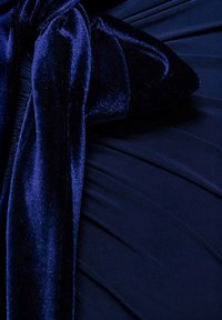 Marineblåt kjolestof med rynket tekstur og en fløjlsbue som accent. Bue er rigt tekstureret og står i kontrast til den glatte satinlignende overflade.