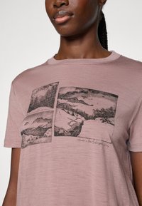Rosa kortermet t-skjorte laget av mykt stoff, med fire svart-hvite landskapstrykk over forsiden og rund hals.