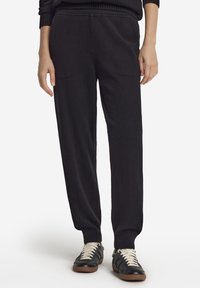 Svarta stickade byxor med avslappnad passform, med ribbad midjeresår och muddar. Matchas med svarta sneakers med vita snören.