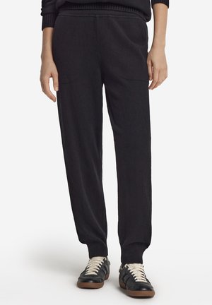 Schwarze Strickhose mit lockerem Sitz, ausgestattet mit einem gerippten Bund und Bündchen. Kombiniert mit schwarzen Sneakern und weißen Schnürsenkeln.