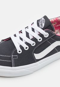 Sneaker Vans neri con lacci bianchi e striscia laterale, fodera interna floreale rosa e logo "Vans Off The Wall" sulla linguetta.