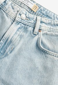 Gai zili džinsi ar bootcut piegriezumu, izgatavoti no denima, ar vidēju vidukļa augstumu, varš pogas aizdari un priekšējām kabatām ar redzamajām šuvēm.