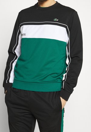 Vihreä ja musta huppari, jossa on valkoisia ja mustia vaakasuoria raitoja, pyöreä kaula-aukko ja Lacoste-logo rinnassa. Pehmeä rakenne.