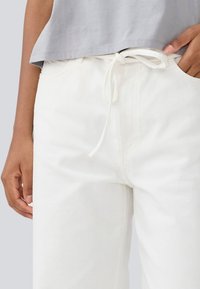 Pantalon en denim blanc avec une coupe décontractée, doté d'une taille élastique à cordon et d'une texture subtile. Associé à un haut gris clair.
