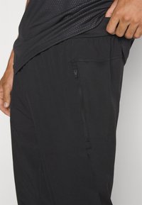 Melni sporta bikses ar elastīgu jostasvietu, ar sānu kabatu ar rāvējslēdzēju un gludu, vieglu audumu.