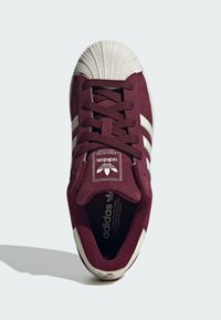 Burgundy suede sneaker with white stripes, rubber shell toe, flat laces, and padded tongue featuring Adidas branding on the insole and tongue.