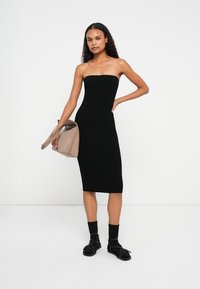 Μαύρο ριμπ πλεκτό strapless midi φόρεμα με εφαρμοστή σιλουέτα. Συνδυασμένο με μπεζ τσάντα και μαύρα σανδάλια με λουριά και κάλτσες.