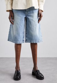 Bermudas de denim en azul claro con un diseño de pierna ancha, dobladillo sin rematar y costuras en contraste. Combinadas con mocasines negros.