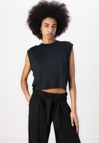 Camiseta sin mangas negra corta con cuello redondo, hecha de una tela suave. Combinada con pantalones negros de cintura alta que cuentan con un cinturón de lazo.