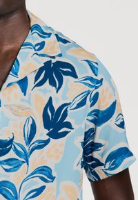 Kortärmad skjorta i ljusblått tyg, med ett blommönster i mörkblå och beige blad. Slät yta och kragadesign.