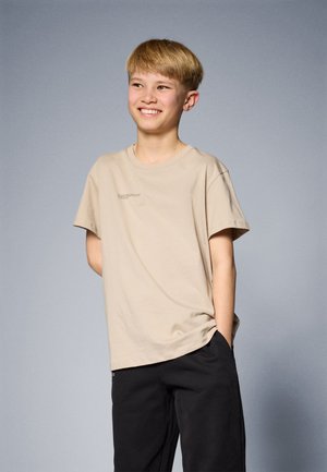 T-shirt en coton beige à manches courtes et à col rond, avec un discret détail textuel à l'avant. Associé à un pantalon noir.