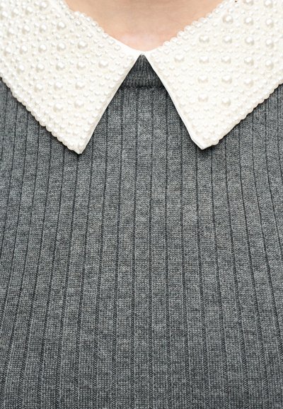 Col à pointe orné de perles blanches sur un pull gris en maille côtelée, visible du cou jusqu'au milieu du torse.