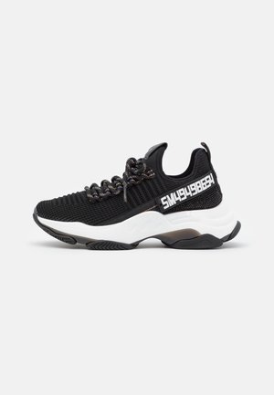Czarny dzianinowy sneaker z masywną białą podeszwą, wielokolorowymi okrągłymi sznurowadłami i białym numerycznym tekstem „SM49498654” na bocznym panelu.