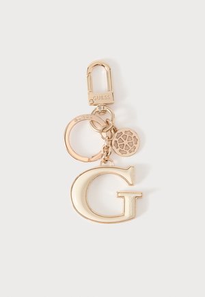 Nøglering i guldfarvet metal med karabin, ring, en rund charm med udskåret mønster, og en stor bogstav G-vedhæng med indgraveret "Guess."