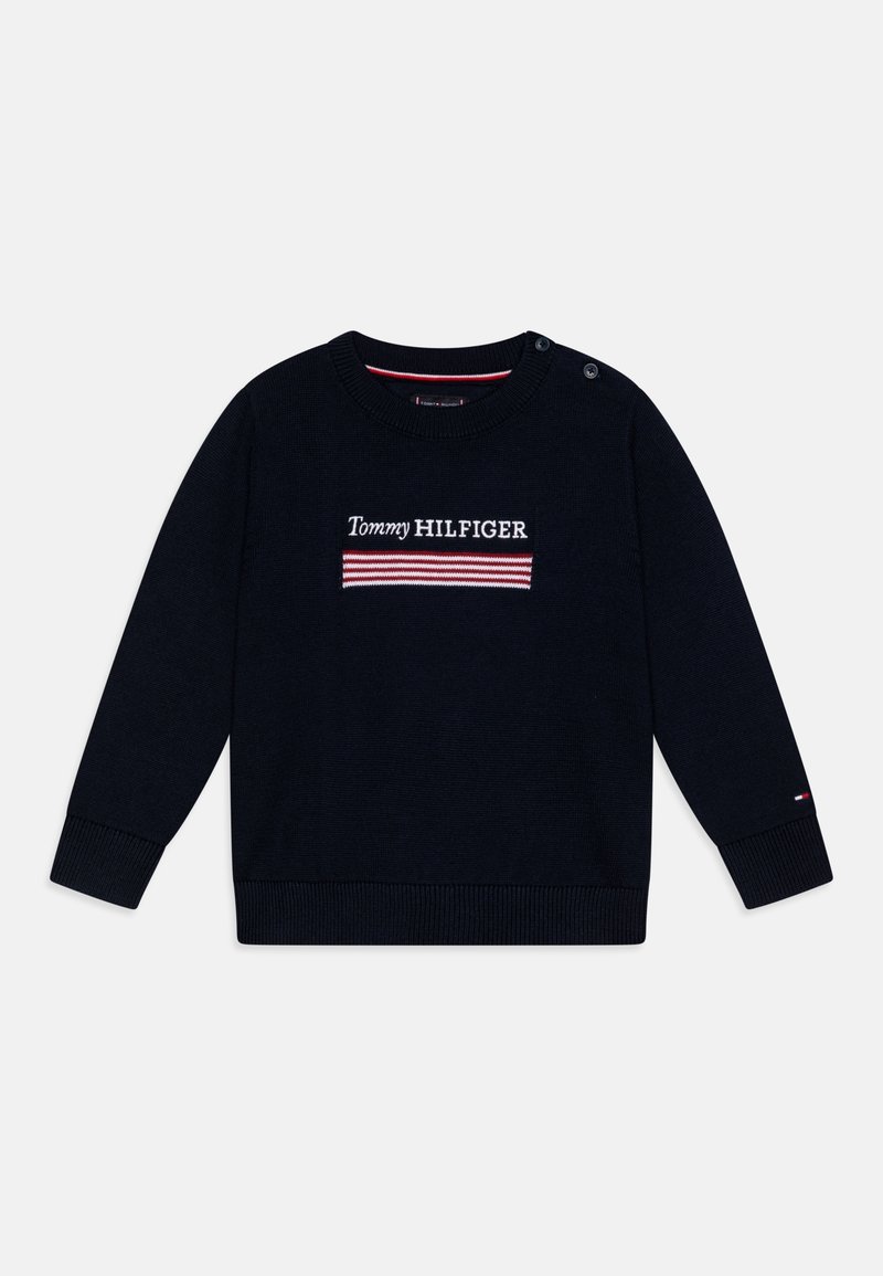 Pull en maille bleu marine à manches longues avec le texte « Tommy Hilfiger » et un motif rayé rouge et blanc sur la poitrine, fermeture par boutons à l'épaule.