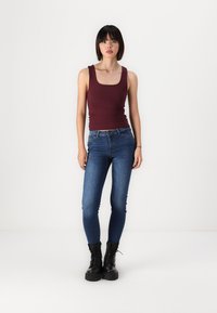 Top en jersey bourgogne ajusté, jeans skinny bleus et bottes à lacets noires. Tissu lisse, design simple et taille régulière.