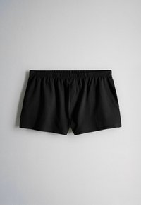 Pantalones cortos negros con cintura elástica, diseño sencillo, colocados planos sobre fondo gris claro.