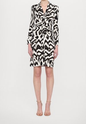 Robe à manches longues à motif noir et blanc, avec fermeture à boutons et ceinture à nouer. Le tissu présente une texture lisse avec un motif géométrique.