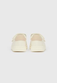 Par kreme barvnih otroških superg s trakovi na ježka, prikazanih od zadaj na belem ozadju.