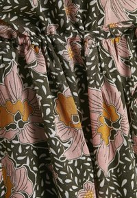 Tissu avec détail de couture froncée montrant une base vert foncé, un motif floral rose et orange, et de petits accents de feuilles blanches.