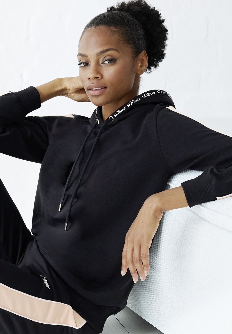 Black hoodie made of soft fabric with a drawstring, featuring a logo-embellished neckline and contrasting light pink side stripes.