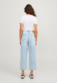 Kvinna sedd bakifrån iklädd en vit kortärmad topp, ljusblå vida jeans och vita sneakers med svarta häldetaljer.