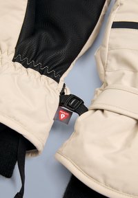 Krämfärgade isolerade handskar med svarta texturerade muddar, utrustade med spänne och röd varumärkesetikett. Slät utsida med elastiska handledsband.