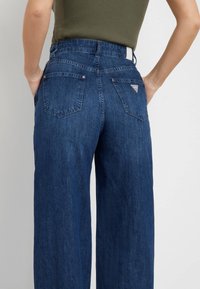 Mörkblå vida jeans med hög midja, med två bakfickor och en liten logodetalj på höger ficka. Denim material.