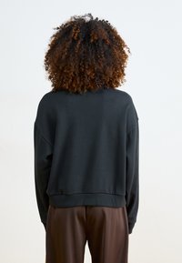 Fekete pulóver, laza szabással, hosszú ujjakkal és bordás aljjal. Puha anyagú textúra, egyszerű dizájn, látható minták vagy logók nélkül.