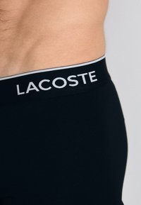 Boxers noirs avec une ceinture douce arborant le logo "LACOSTE" en blanc. Le matériau semble lisse et extensible.