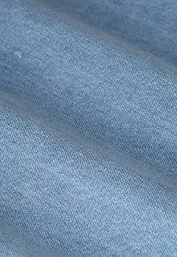 Tissu en denim bleu clair avec une texture de tissage visible et de douces plis.