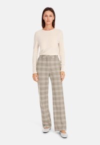 Light beige sweater with long sleeves, paired with high-waisted plaid trousers in muted tones of gray and beige. Simple flat shoes.