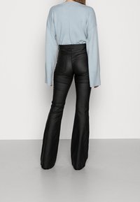 Pull oversize bleu clair à manches larges associé à un pantalon évasé noir en similicuir taille haute, vue de dos avec détails des coutures.