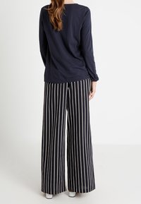 Námořnicky modrý top s dlouhým rukávem spojený s černobílými pruhovanými kalhotami s širokými nohavicemi. Kalhoty mají šňůrkový pas a jemnou texturu.