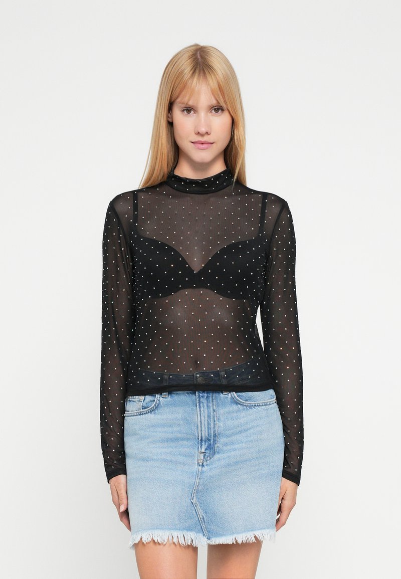 Sort netbluse med lange ærmer og høj hals, pyntet med sølvfarvede polkaprikker, lagdelt over en sort bh, kombineret med en lys denim mininederdel.