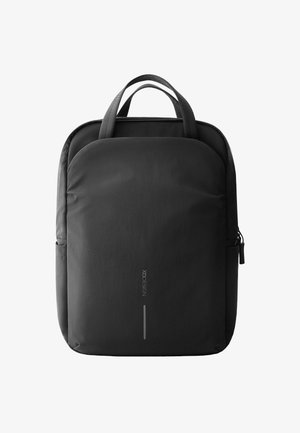 Mochila de nylon negra con una textura suave, que presenta dos asas superiores, un bolsillo lateral y un detalle de logo reflectante en la parte frontal.