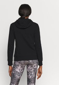 Sudadera negra con un bolsillo frontal y capucha ajustable con cordón, combinada con leggings gris con estampado de leopardo. Textura suave y diseño ajustado.
