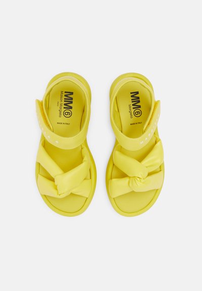 Κίτρινες σάντες με σχέδιο κόμπου, κατασκευασμένες από μια λεία, ευέλικτη ύλη. Διαθέτουν ρυθμιζόμενες λουρίδες και αντιολισθητική σόλα.