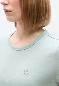 Φωτεινό πράσινο μπλουζάκι με στρογγυλή λαιμόκοψη. Διαθέτει κεντημένο λογότυπο στο στήθος. Κατασκευασμένο από λείο, απαλό ύφασμα.