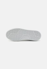 Semelle de chaussure blanche avec une adhérence texturée, arborant un design géométrique. Des bords lisses et un détail de logo subtil au centre rehaussent l'apparence.